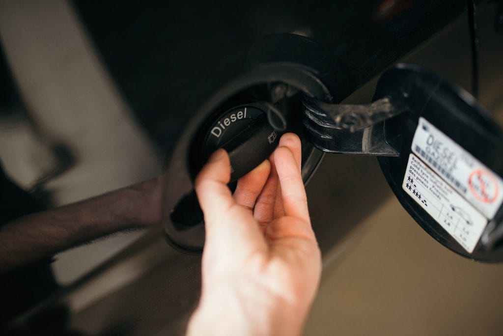 Refueling a diesel vehicle at a gas station during the day with focus on the fuel cap and nozzle